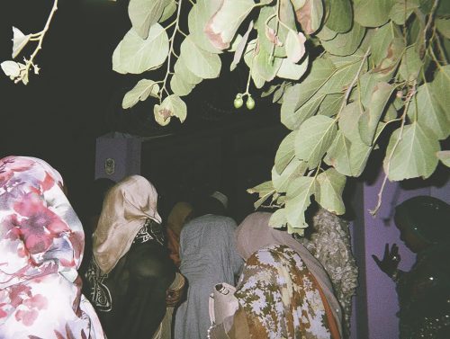A group of Sudanese women walk through purple doors in the evening