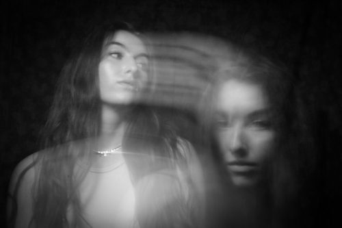 This black and white image features the same fair skinned female. On the left side of the image she sits looking across the frame. Coming from her face are motion blur streaks which lead to a ghostly image of her face in the right bottom corner of the frame.