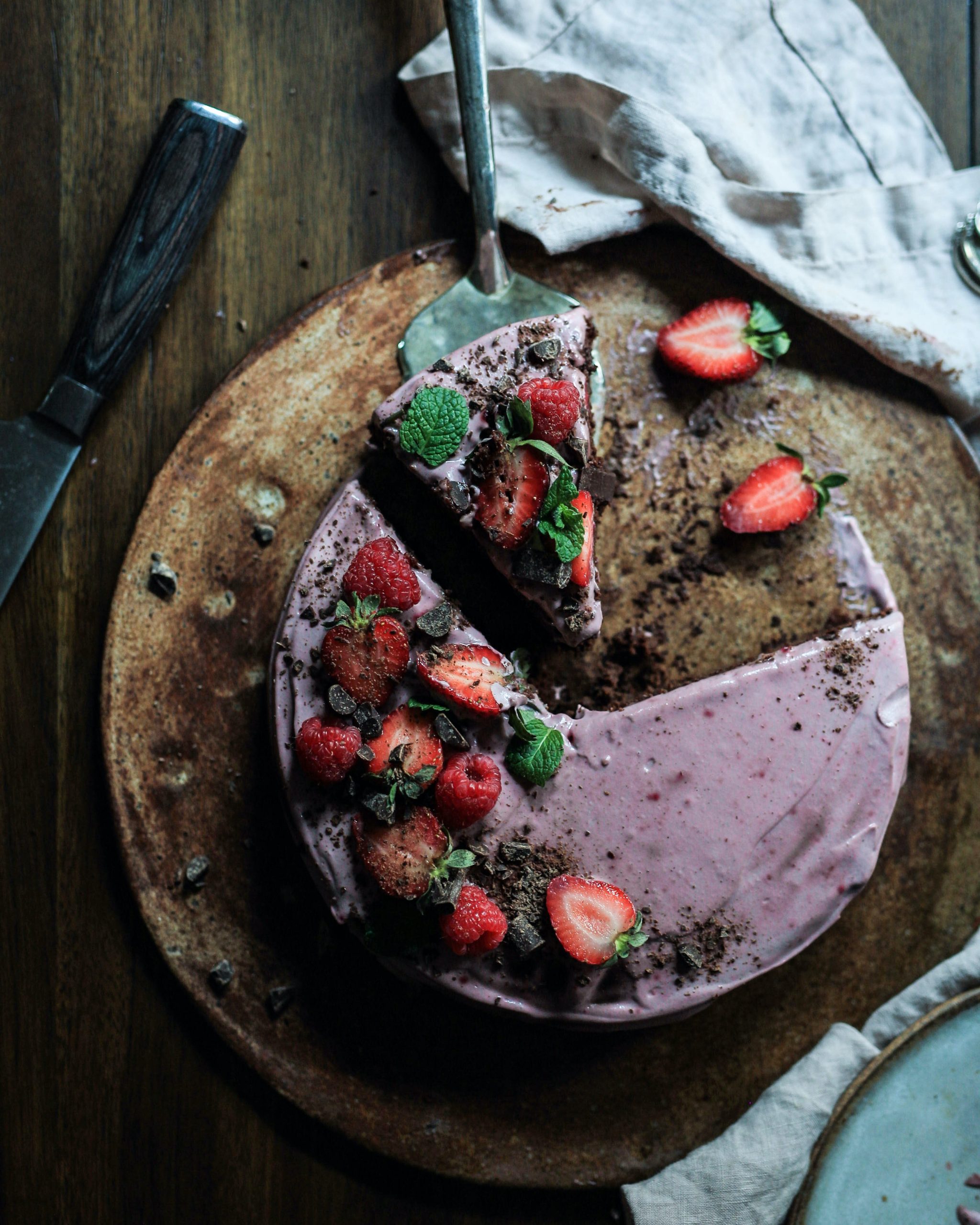 color photograph of a partially sliced chocolate cake with purple frosting and strawberries